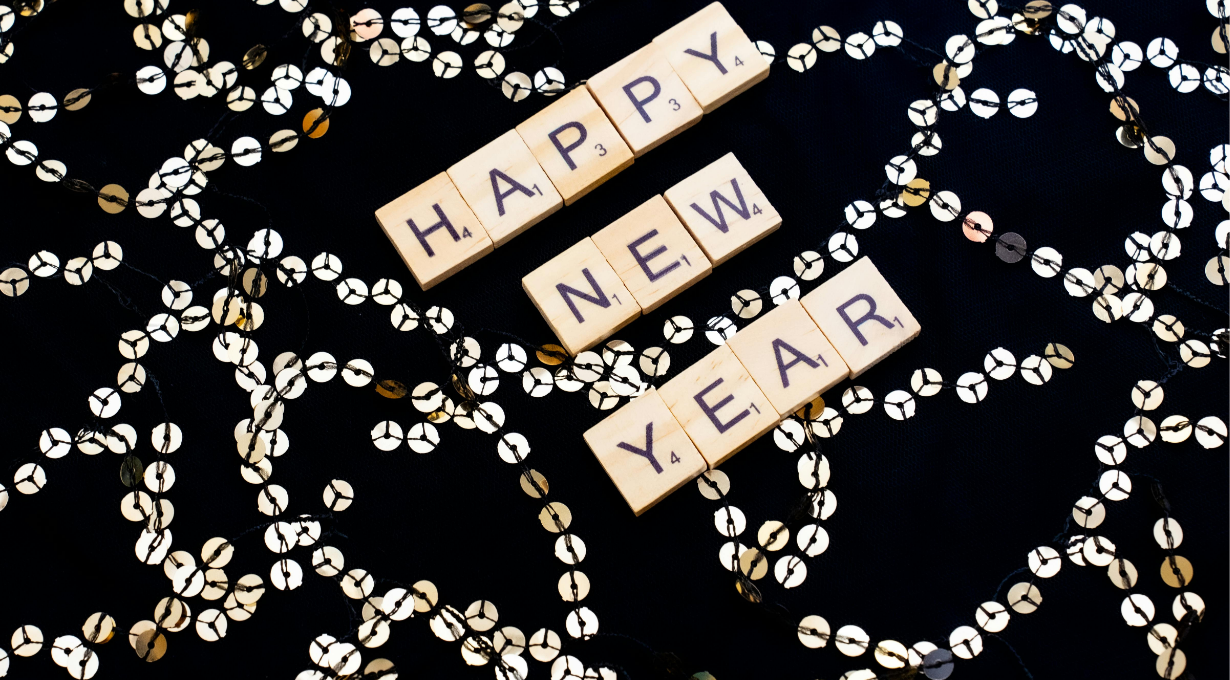 Scrabble tiles spelling out Happy New Year on a black background surrounded by gold sequin garland, happy new year wishes